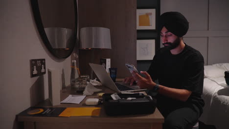 stressed man browsing on mobile phone in front of his laptop in the bedroom