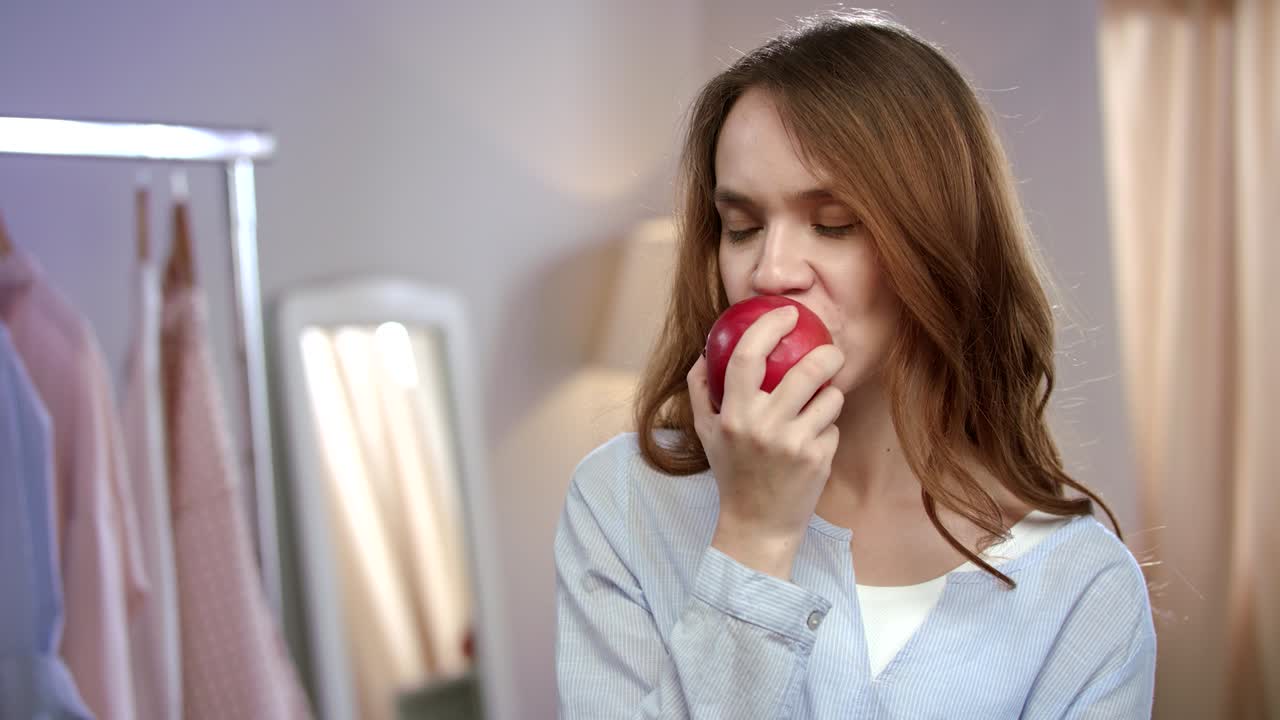 Portrait of cheerful woman eating red apple at home. Healthy woman eating fruit
