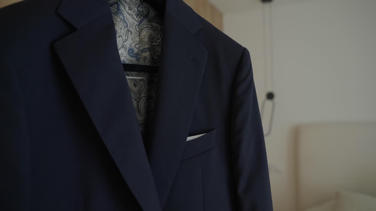 Vista ravvicinata di una giacca da abito formale blu scuro con gilet a fantasia e fazzoletto da taschino bianco, preparata per la cerimonia nuziale.
