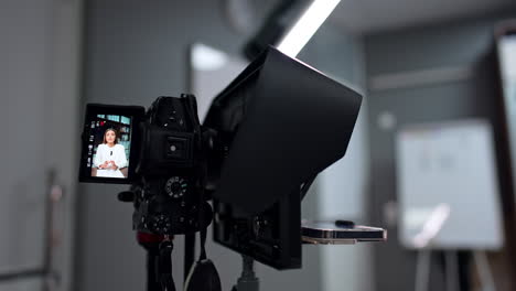 working professional camera on tripod filming a female speaker. close up. smartphone attached to camera to show the subtitles. blogging concept.