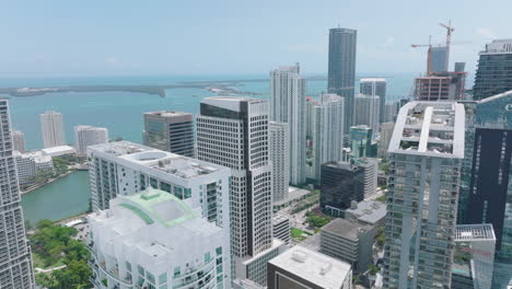 Aerial-view-of-downtown-skyscrapers-on-sunny-day.-Slide-and-pan-shot-of-modern-high-rise-office-or-apartment-buildings-and-water-in-background.-Miami,-USA