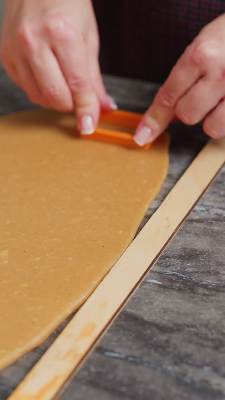 primer plano de una mujer cortando la masa usando una herramienta de horneado, manos presionando un cortador de galletas naranja, rodillo de madera al lado, masa bien enrollada, pulsera de cuentas rosas en la muñeca