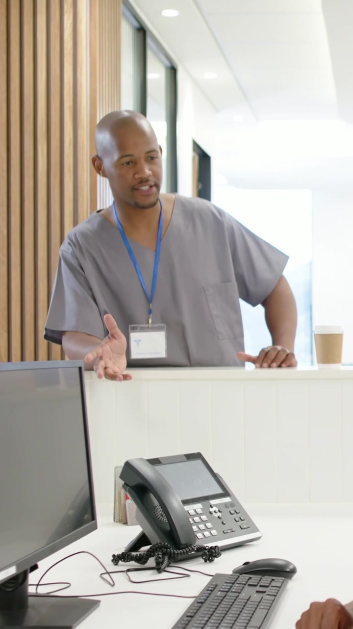 Video verticale: Personale in camice medico con badge blu che cammina, si appoggia alla scrivania della clinica e discute il check-in.