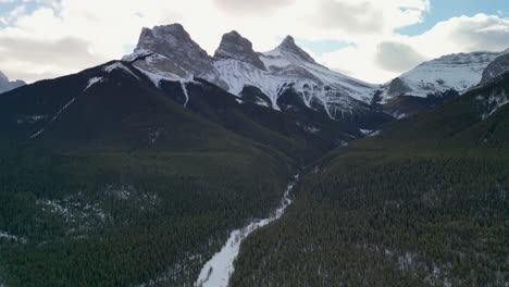 vista aérea del pico de la montaña de las tres hermanas con el valle y el bosque, alberta, canadá - dron 4k