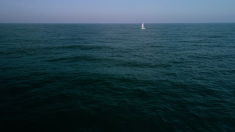 drone shot travelling out to sea towards a sailing boat towing a dinghy and sweeping round to see land in the back ground