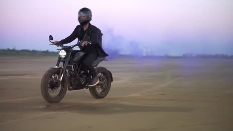 Young-biker-in-black-riding-while-the-engine-blowing-out-blue-exhaust-smoke,-holi