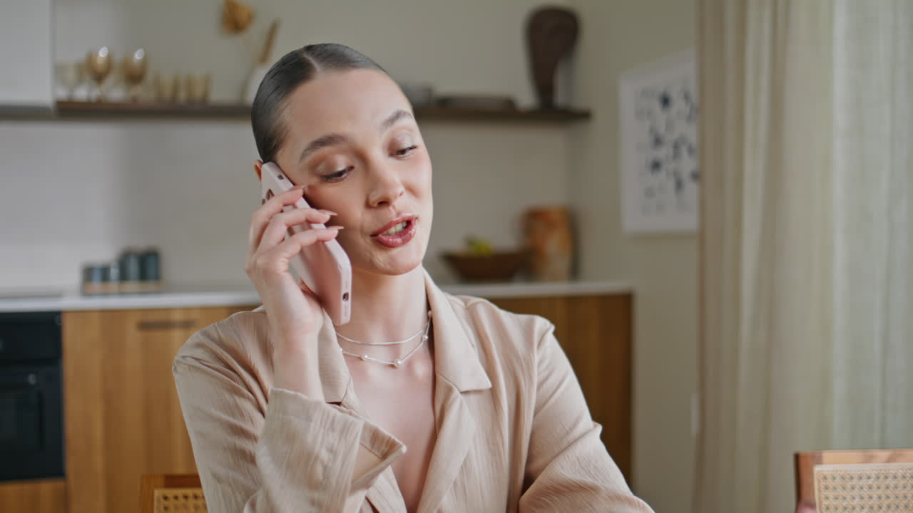 Smiling girl speaking smartphone looking manicure at apartment kitchen closeup