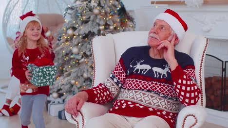 granddaughter gifting christmas xmas present box to amazed happy grandfather at home, celebrating