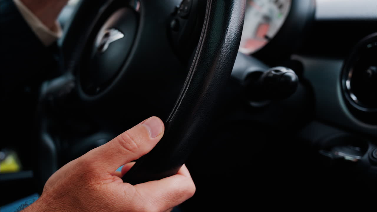 Close up of a man's hands on a steering wheel, driving a car on the road in the rain