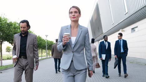 junge kaukasische glückliche geschäftsfrau, die die straße entlang geht und morgens eine kaffeetasse hält