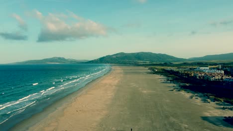 Ein-Endloser-Strand-In-Einer-Filmischen-Luftaufnahme-Mit-Wellen,-Hügeln-Und-Blauem-Himmel