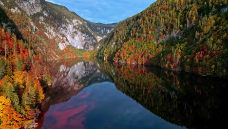 Aerial-view-of-a-calm-lake-reflecting-colorful-autumn-trees-and-steep-cliffs-on-a-cloudy-day