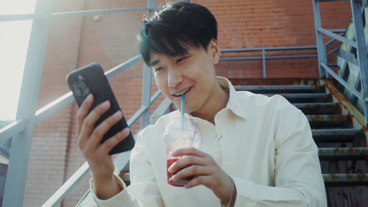 계단 에서 스무디 를 마시면서 스마트폰 을 사용 하는 젊은 남자
