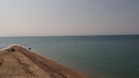 backwards revealing aerial drone shot of a peninsula that extends into the ocean over a golden sandy shore and the blue sea of mediterranean sea close to thessaloniki, greece in epanomi