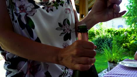 mujer abriendo una botella de champán en una fiesta en el jardín