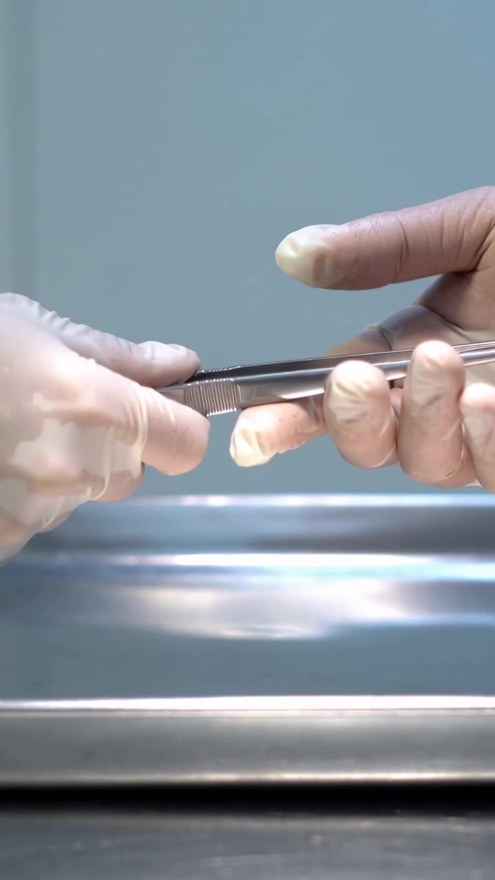 Vídeo vertical: Pinças em movimento, mãos enluvadas alinhando e entregando um gancho sobre um dedo em uma bandeja de clínica