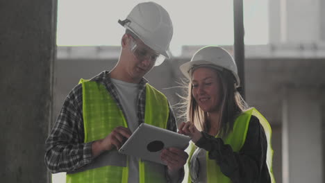 trabajador de la construcción hombre y arquitecto mujer en un casco discutir el plan de construcción de la casa hablar el uno al otro sobre el diseño sosteniendo una tableta mirar los dibujos fondo de los rayos del sol.