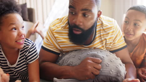 father and children lying on bed, using tablet and enjoying african american family time