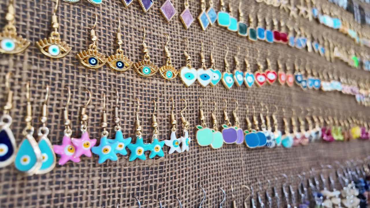 A close-up view of a diverse collection of colorful earrings displayed on a textured burlap-like fabric