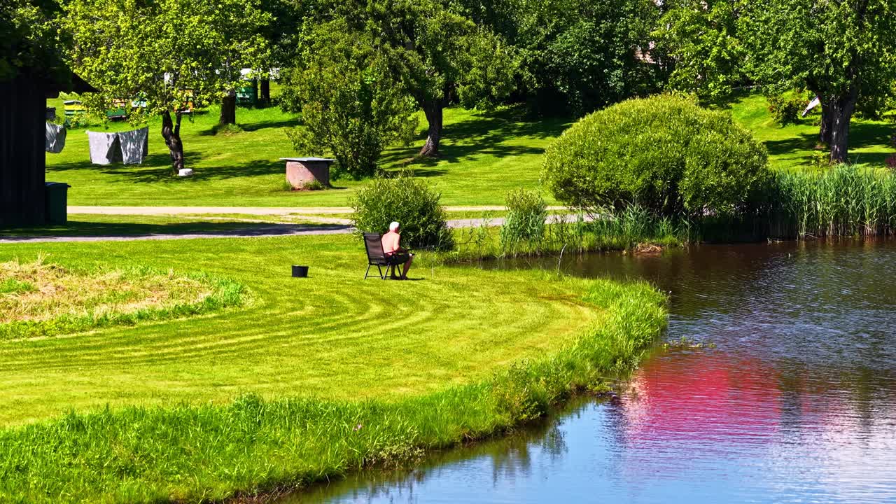 Cinematic shot of an old man sitting on a bench in a grassy field on a sunny day
