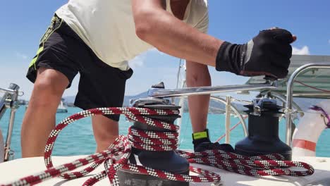 man operating a winch on a sailboat