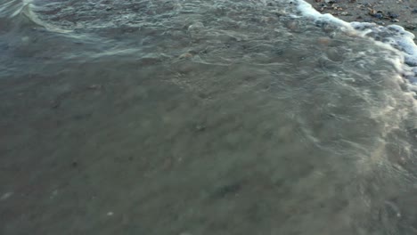 ocean tide washing ashore over beach full of seashells, slow motion