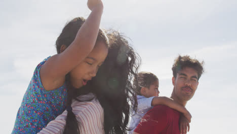 padres hispanos felices cargando a sus hijos en una mochila y caminando por la playa