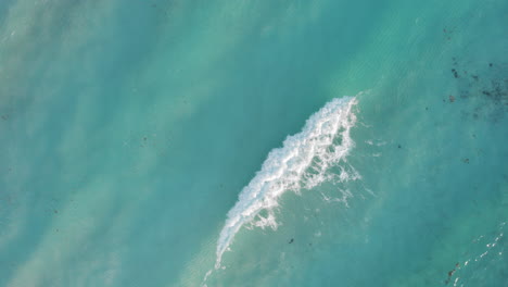 Aerial-top-down-shot-of-rolling-waves-in-a-crystal-clear-blue-ocean-in-Cancun-Mexico