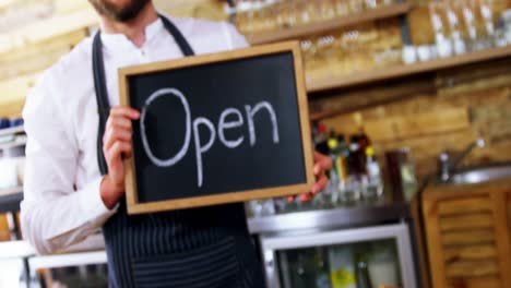 smiling waiter holding open sign board