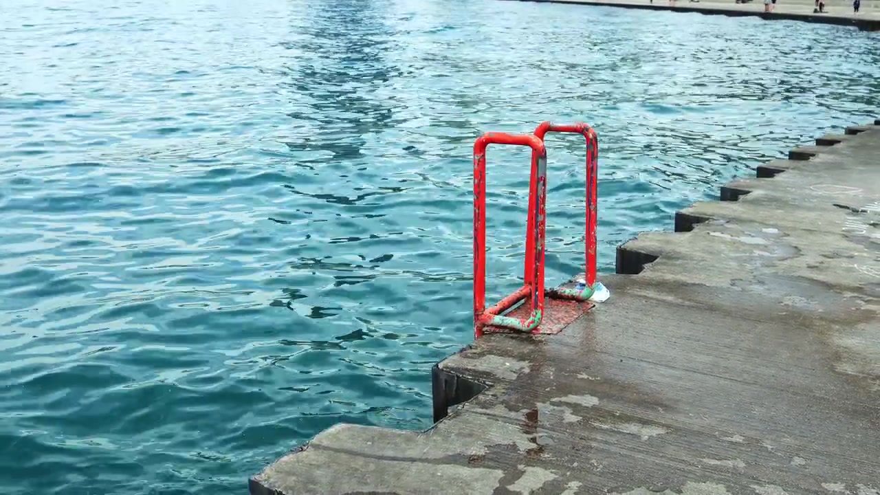 Red railing at the edge of a concrete pier by the water during daytime with reflections on the surface and a calm atmosphere