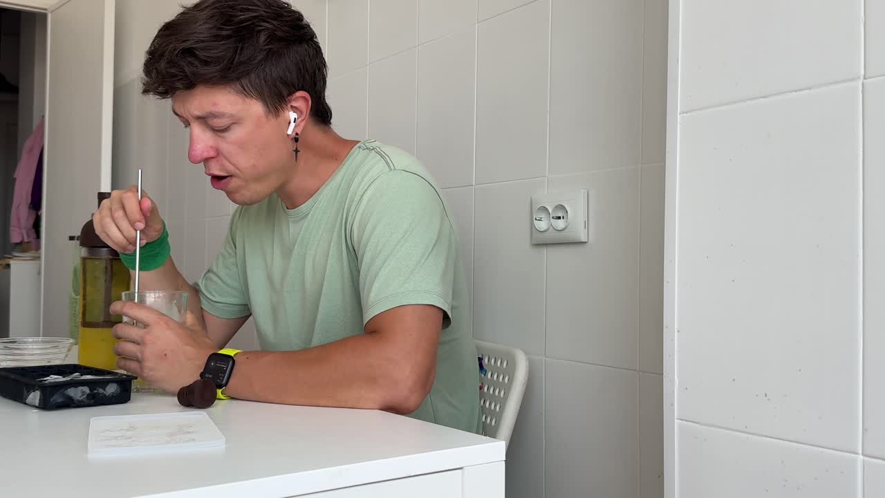 Young Man Preparing and Drinking a Cold Beverage with Ice in Kitchen
