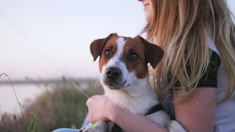 young happy woman and het little dog sitting with flying kite on a glade at sunset