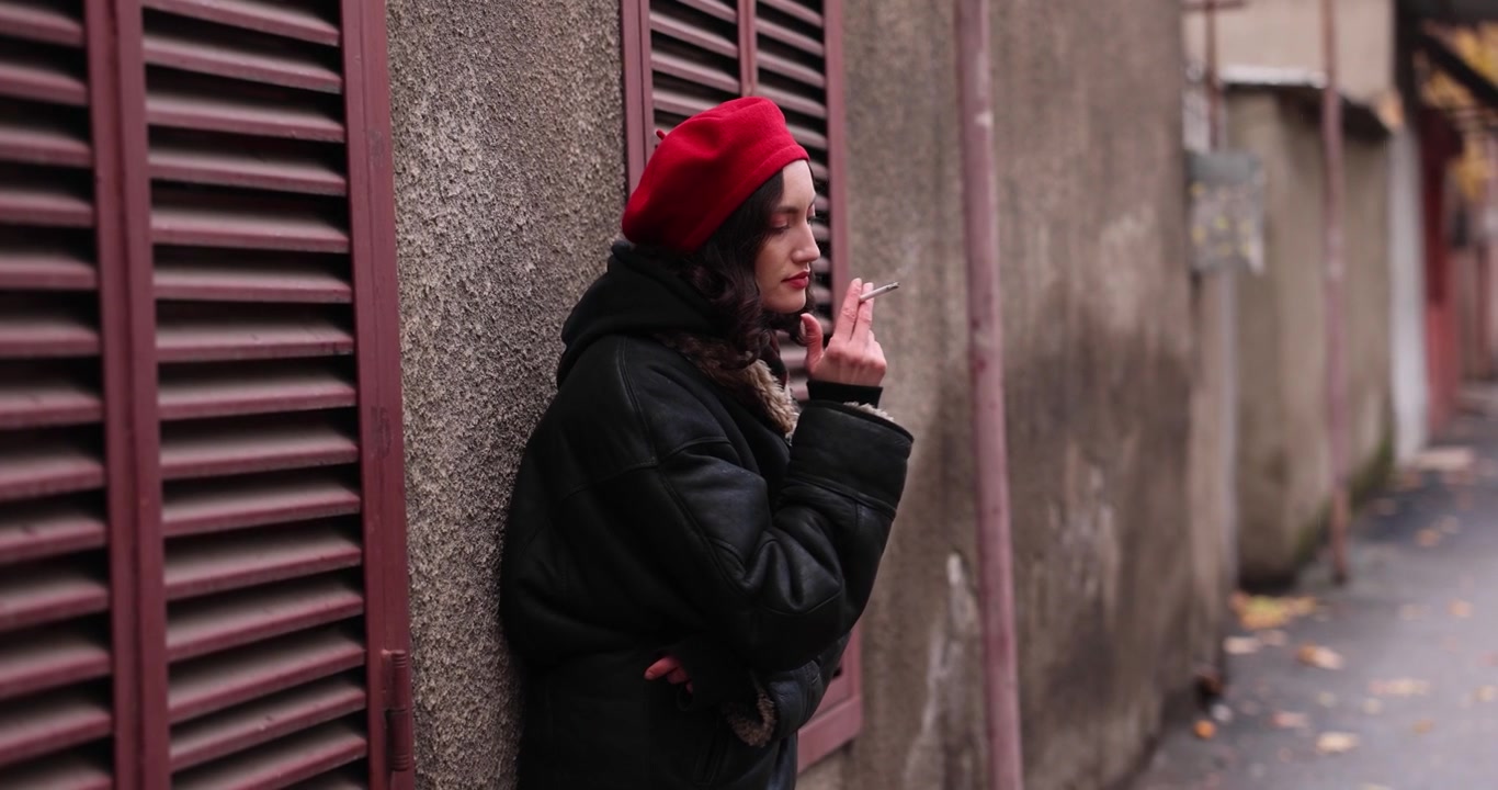 Giovane donna elegante con basco rosso fuma una sigaretta per strada.