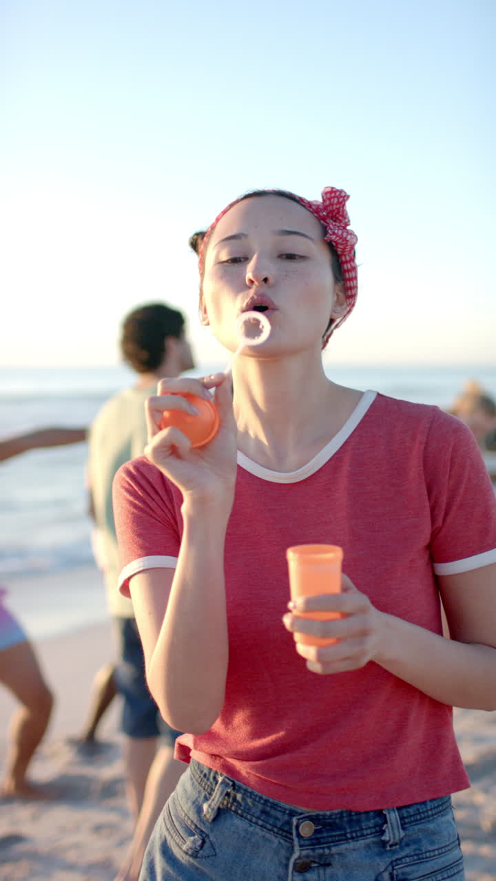 Vertical video: Blowing bubbles at beach, woman enjoying summer evening with friends