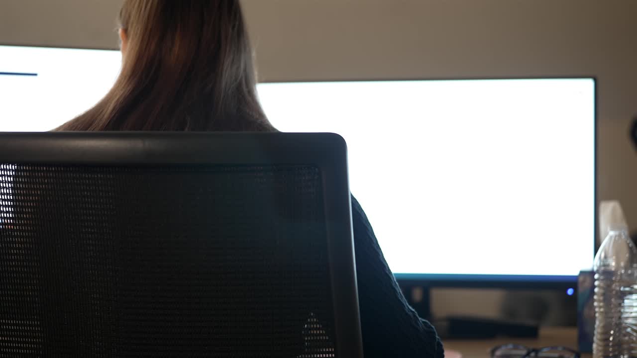 Woman Deep in Work on Modern PC Setup, Back View