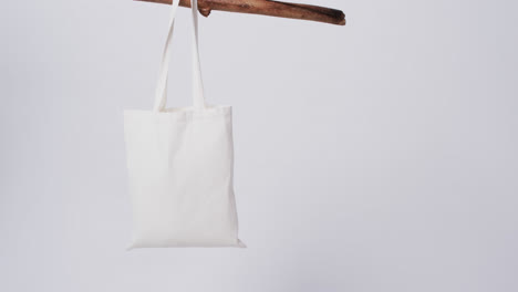 video of white canvas bag hanging from branch with copy space on white background