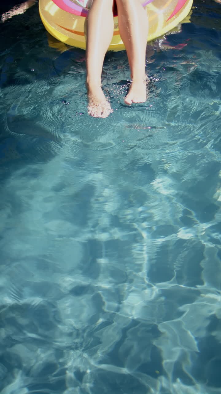 Vertical video: Relaxing in pool, teenage girl's feet dipping in water, enjoying summer day