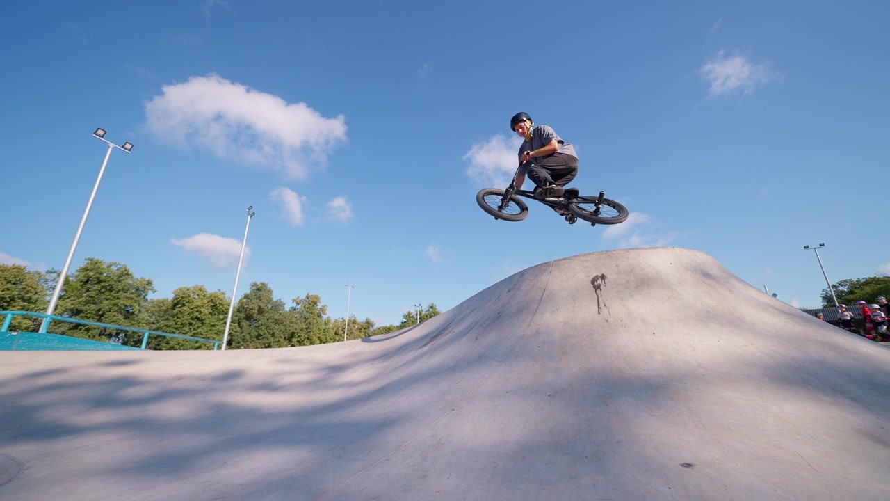 Ung mand på BMX-cykel springer over en betonrampe i en skatepark
