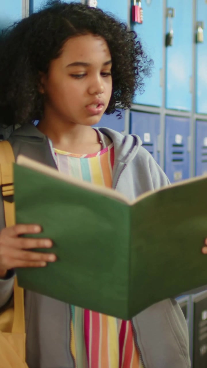 Vertical video: Opening green folder, teen rehearsing at blue lockers, wearing hoodie and backpack