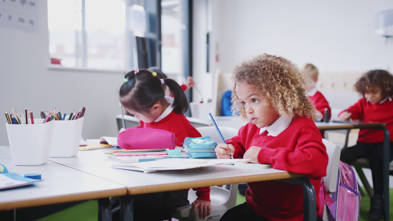 chicas jóvenes en uniformes escolares trabajando en un escritorio en un aula de escuela infantil, de cerca, bajo ángulo