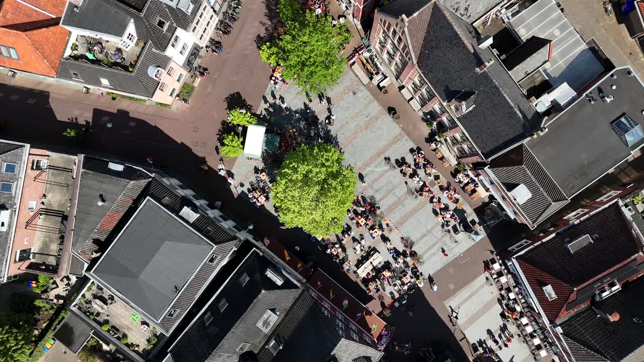 Relaxing people and pedestrian in dutch city during Kings Day. Aerial top down landing. Sunny day in dutch market center square. Green tree in spring. Celebration King Willem Alexander at Koningsdag
