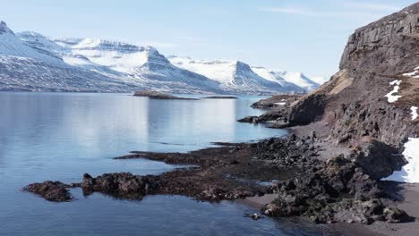 Natural-fjord-landscape-with-rocky-shore-and-distant-mountains-in-Iceland,-aerial