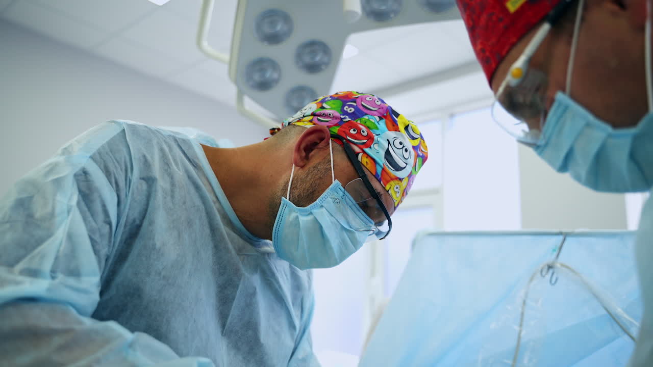 Surgeons in funny colorful caps working at surgical operation. Doctors performing surgery in modern hospital. Low angle view.