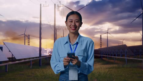 asian female with her smarphone with solar panel and wind turbines, she is looking at the camera with a smile