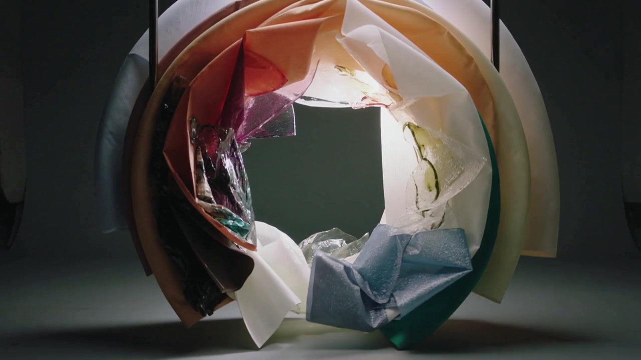 Rotolo circolare che si srotola su un supporto da tavolo a due aste dopo l'avvio, rivelando una retroilluminazione, con un frammento che si deposita.