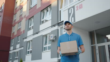 Blue-delivery-man-send-a-package-to-customer-on-before-deliver-cargo.-4k-resolution-and-slow-motion-shot.-Male-postman-with-parcel-in-hands-at-city-street.-Postal-concept.-Delivery-service.