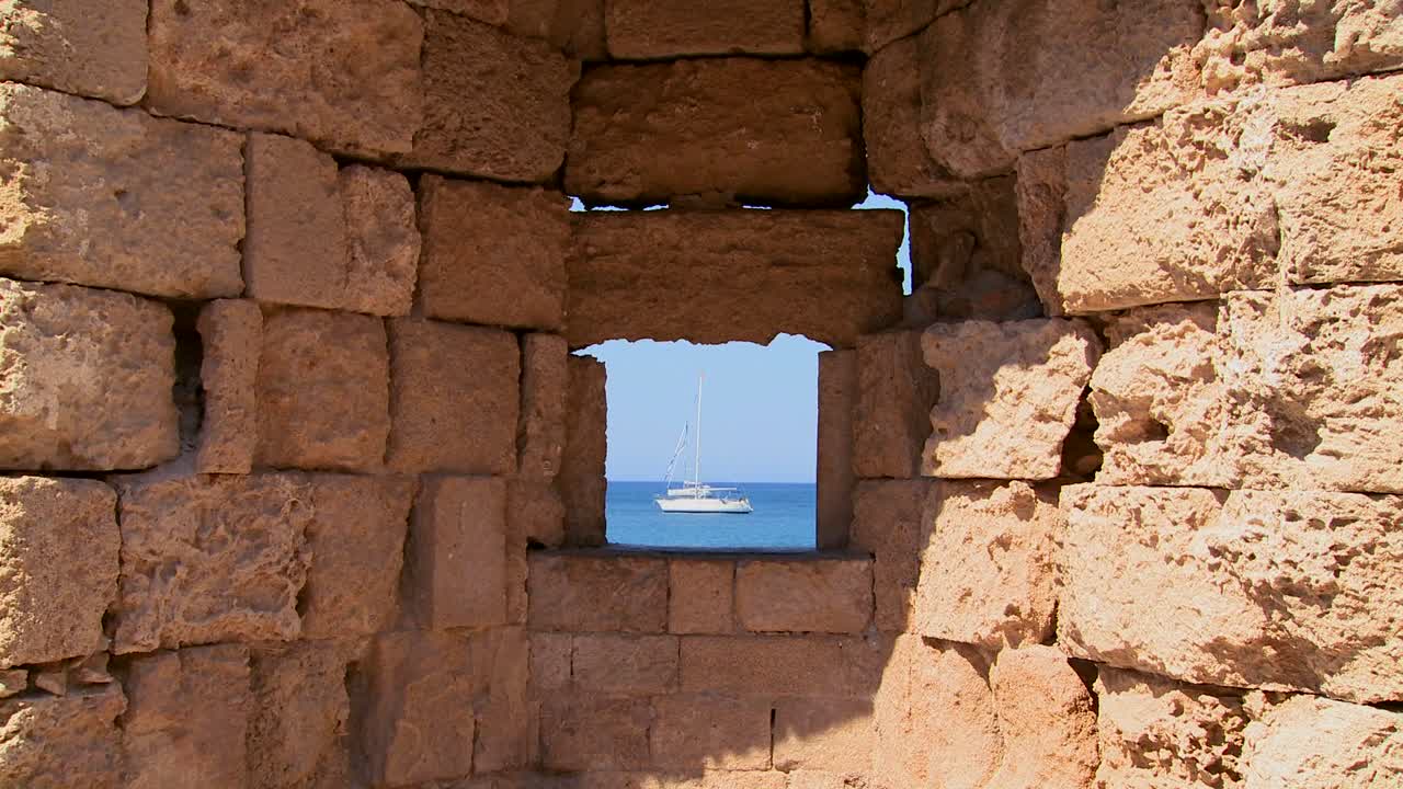 un velero está perfectamente enmarcado a través de un muro del castillo en rodas, grecia
