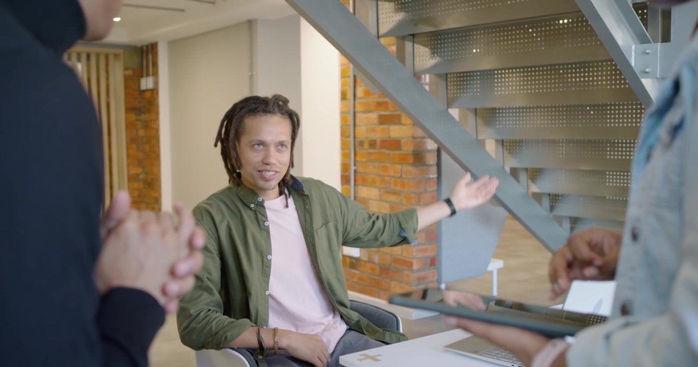 African team meeting with seated man raising hands explaining at desk while colleague with tablet