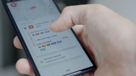 Scrolling-through-the-smart-mobility-app-on-a-black-cell-phone,-planning-public-transport,-illustrative-editorial