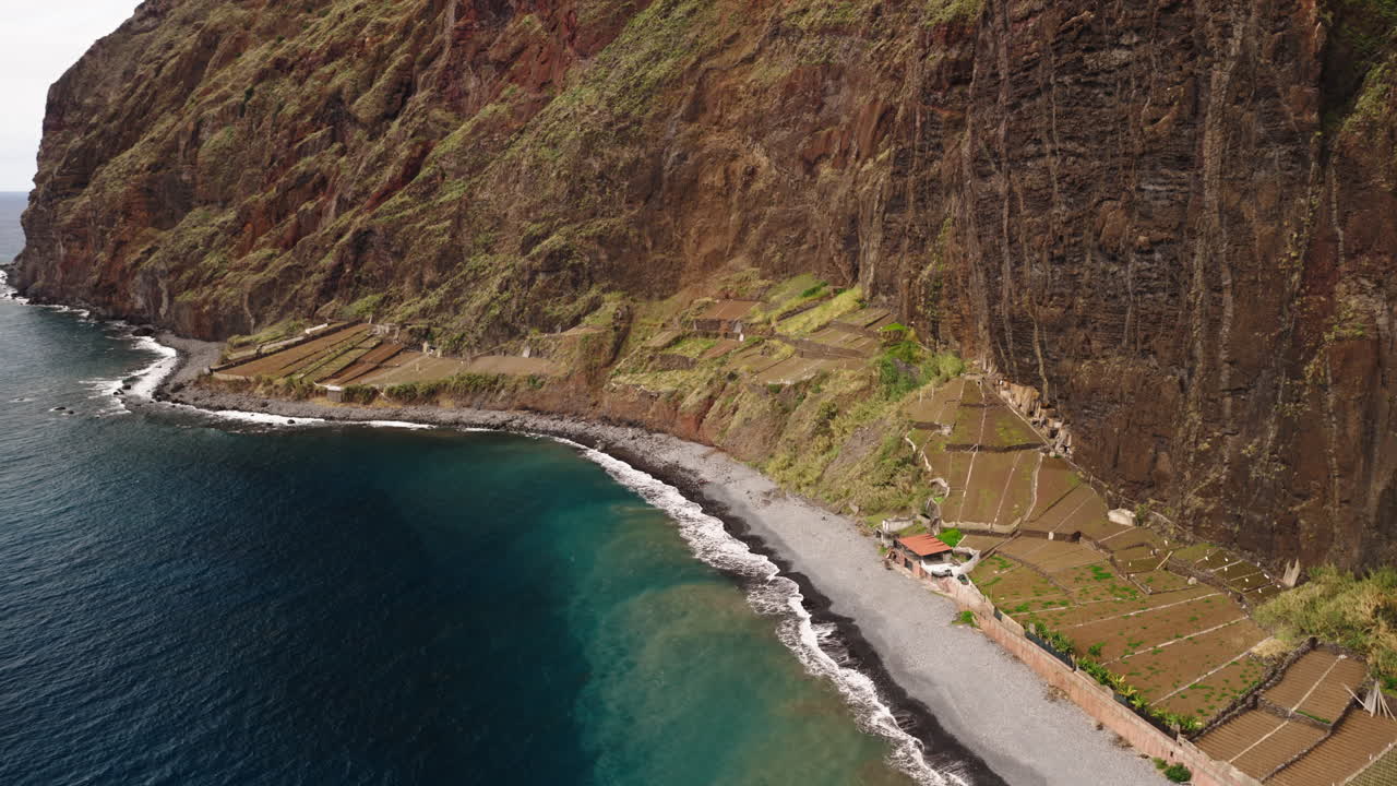 Vista aérea de un acantilado costero con terrazas agrícolas y playa de guijarros